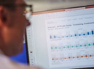 A person is looking at a computer screen displaying a document titled 'Overview - All Private Equity - Fundraising, Investments, & D'. The document contains statistical charts and graphs related to private equity market statistics from 2007 to 2022. Various tabs and functions like 'File', 'Home', 'Insert', and 'Design' are visible in the interface.